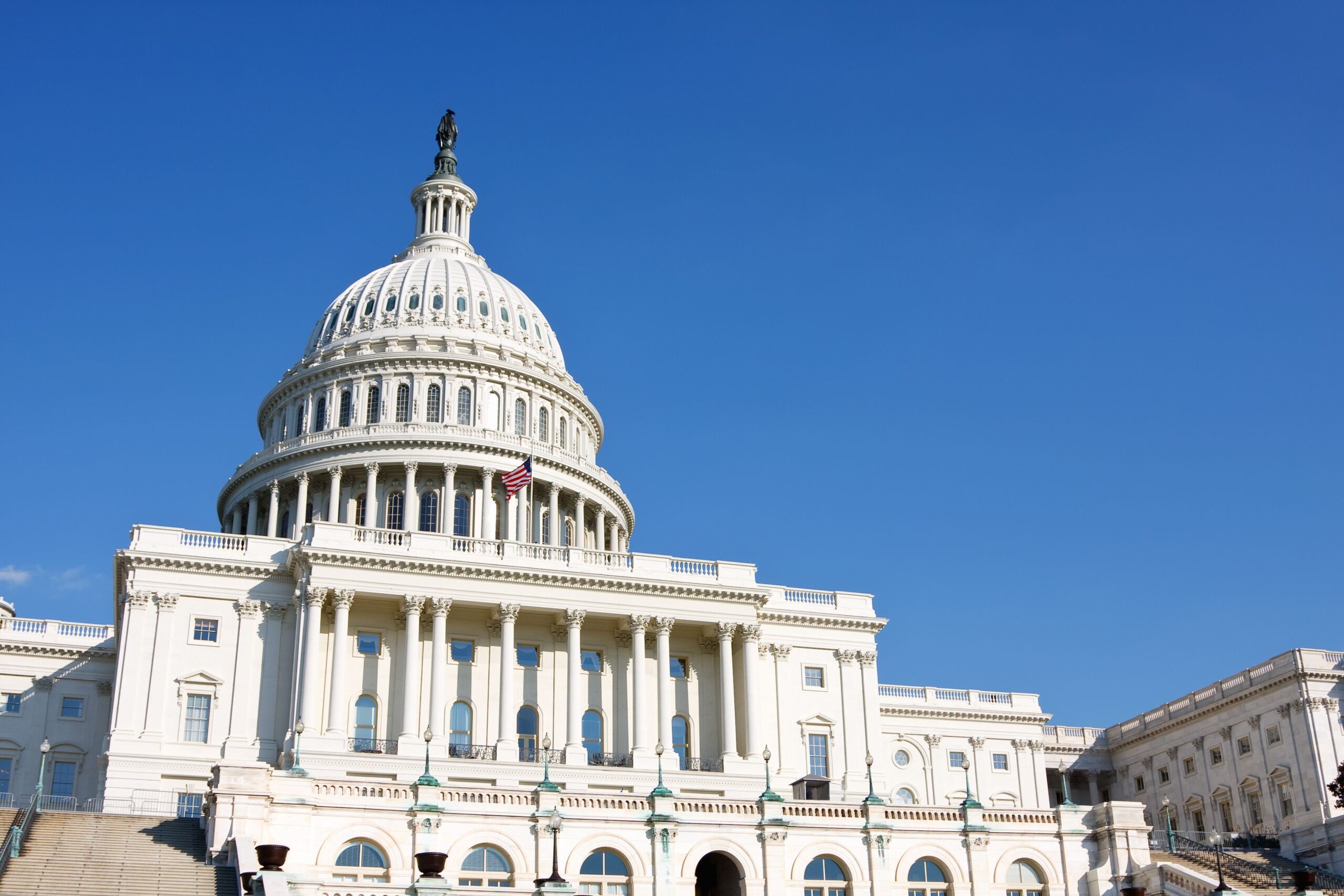 The United States Capitol building, a neoclassical structure, features a large dome and is surrounded by green lawns and trees.