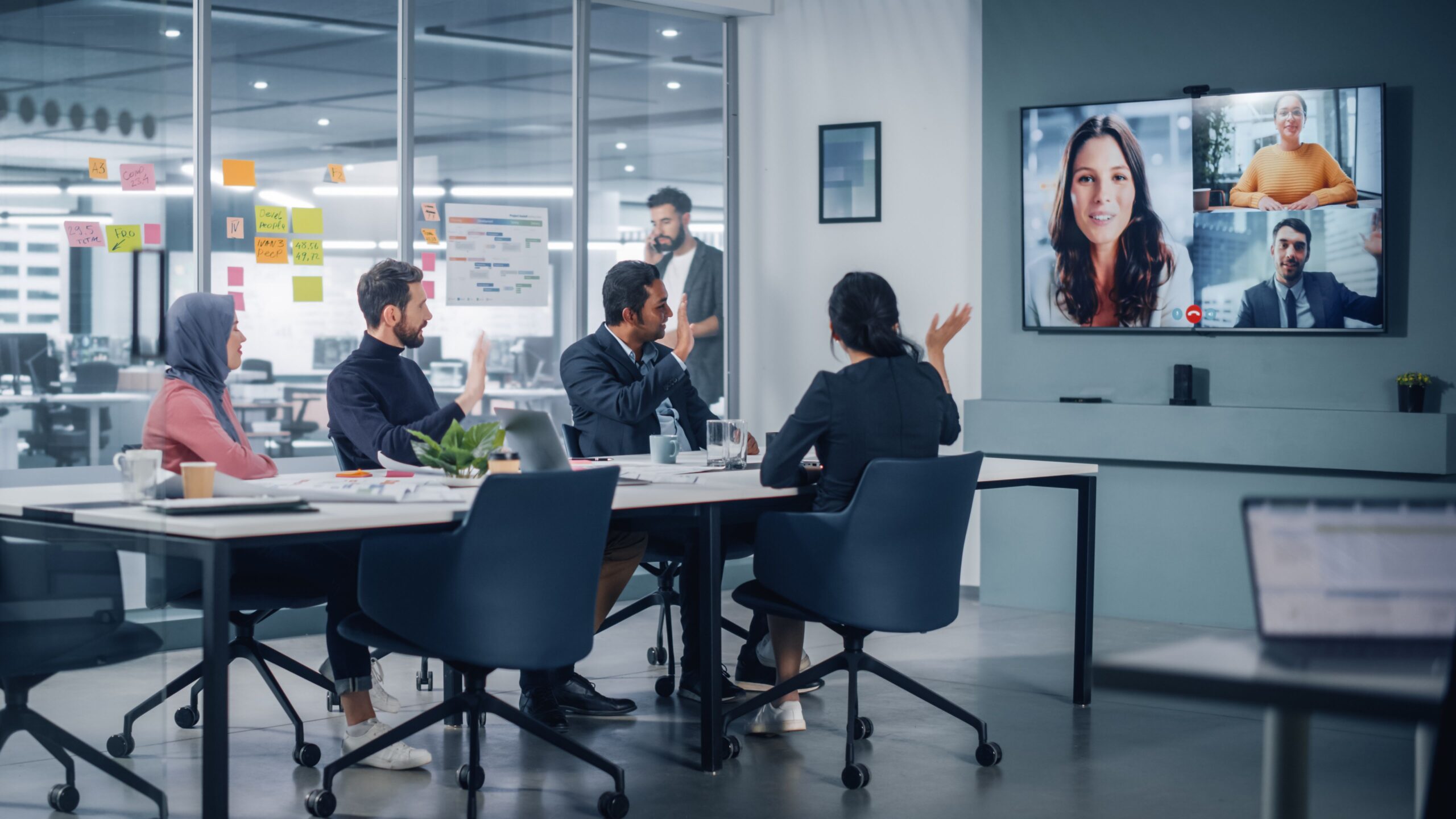 A diverse group of professionals gathered in a meeting room, focused on a large screen displaying presentation content.