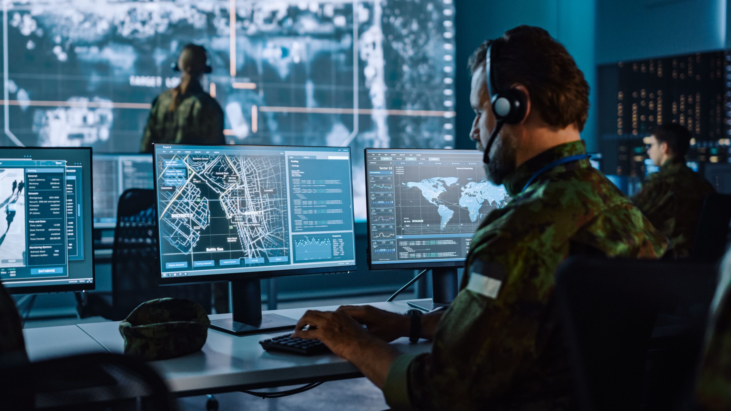 Military personnel focused on computers in a workspace, collaborating on tasks and analyzing data