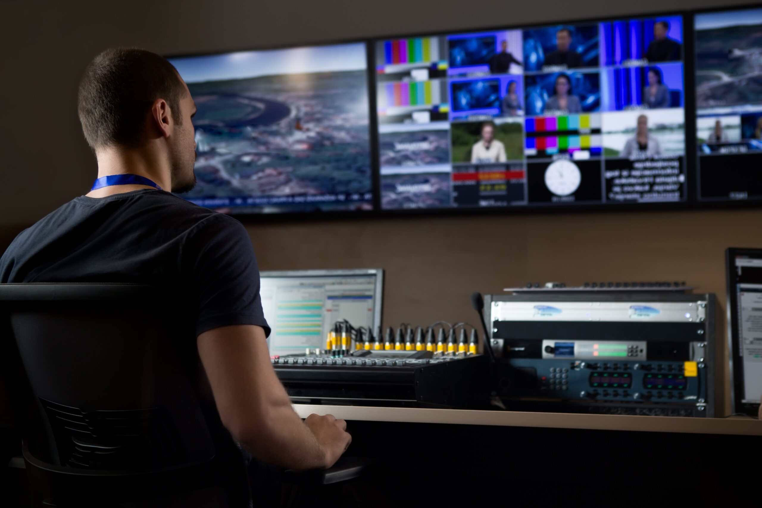 A man seated at a desk, focused on multiple computer monitors displaying various applications and data.