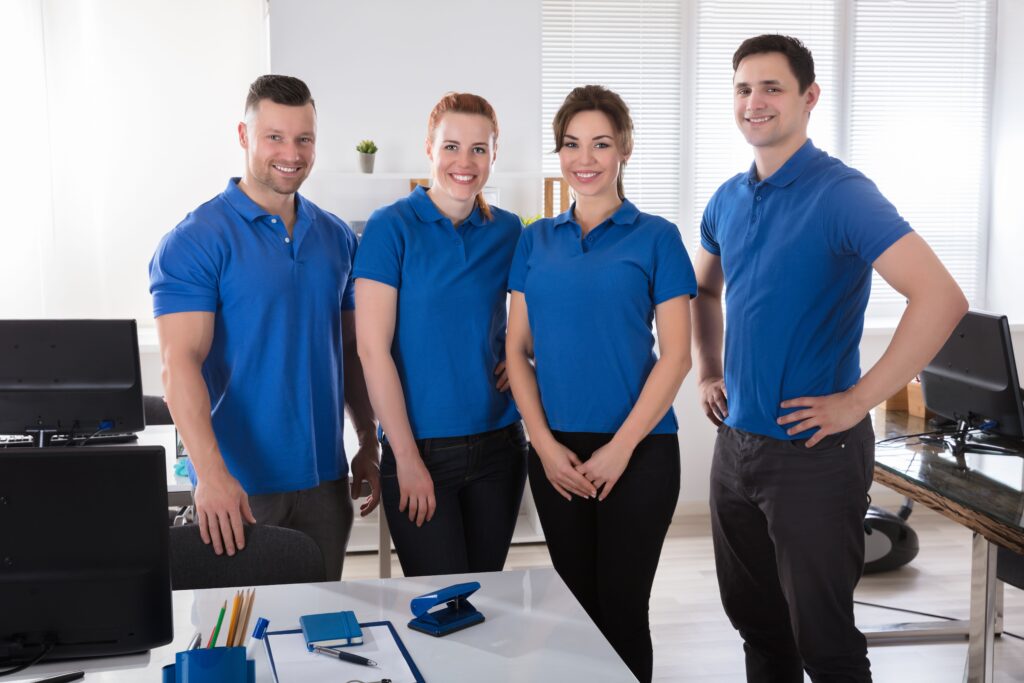 Three individuals in blue shirts stand in front of a desk, engaged in conversation or collaboration
